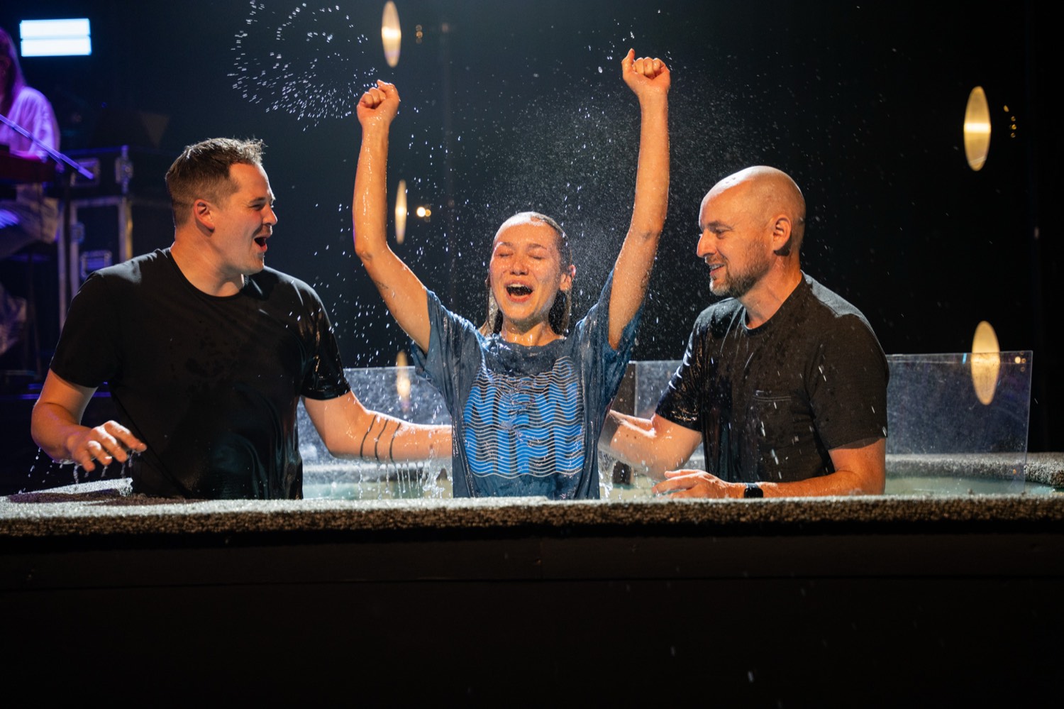 A woman coming up out of the baptism tank with both arms raised